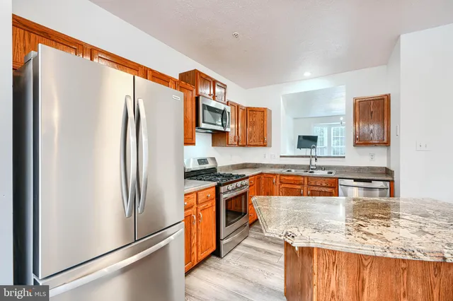 a kitchen with stainless steel appliances granite countertop a refrigerator a stove and a sink with wooden floor