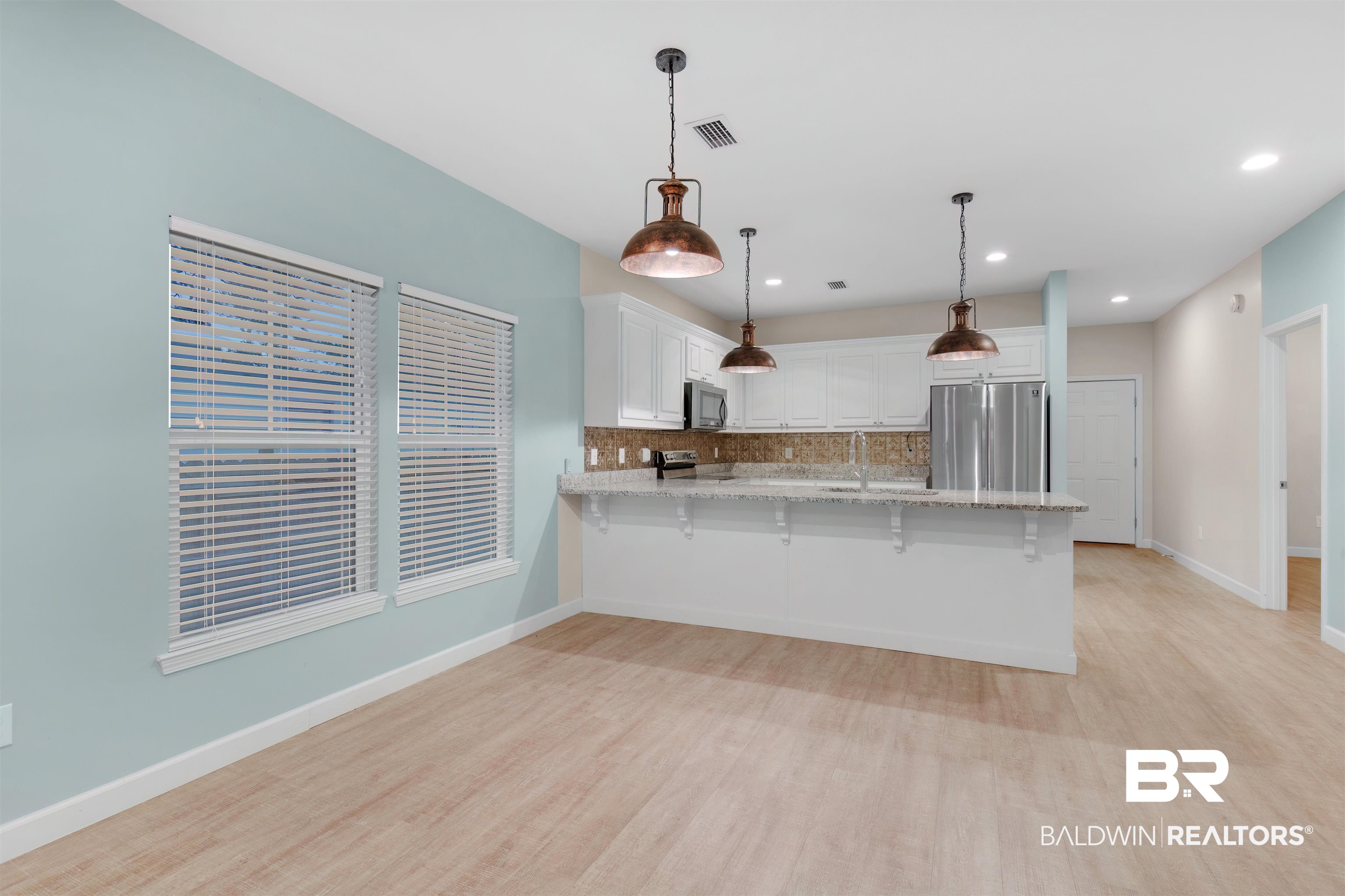 5625 Georgia Street Orange Beach, AL 36561 - Photo 10 of 30 Kitchen with stainless steel appliances, white cabinetry, backsplash, and pendant lighting