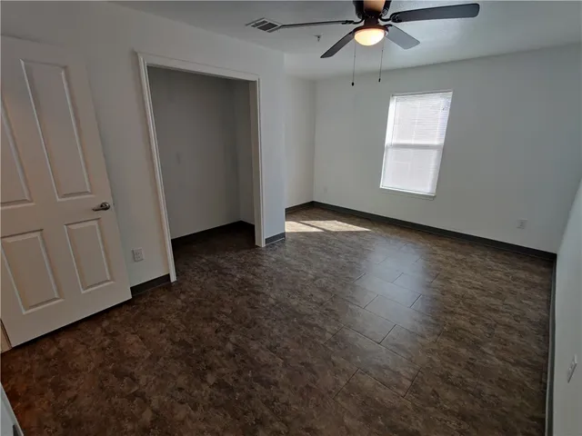 an empty room with wooden floor fan and windows