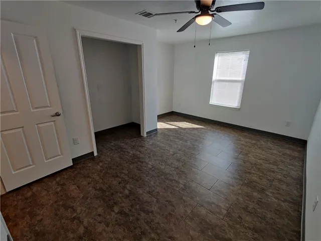 an empty room with wooden floor fan and windows