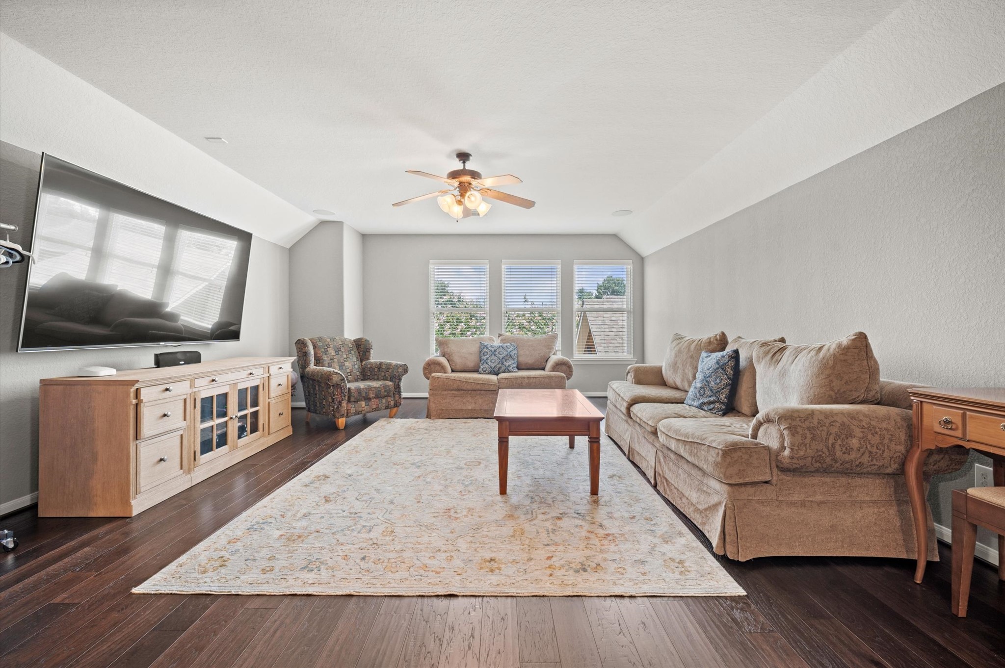 9507 Empress Crossing Drive Spring, TX 77379 - Photo 33 of 50 This living room is spacious and bright, featuring hardwood floors and a large window that lets in natural light. It includes a comfortable seating area with two sofas and an armchair, a ceiling fan, a mounted flat-screen TV, and a wooden entertainment console, creating a cozy and inviting atmosphere.