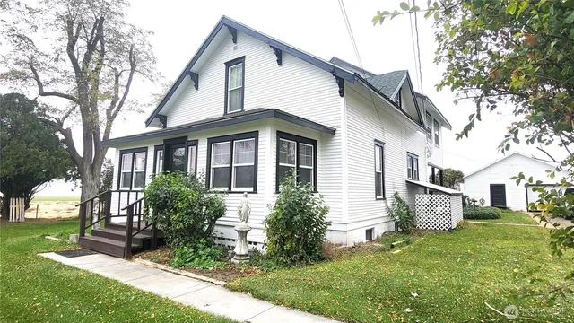 a view of a white house next to a yard with big trees