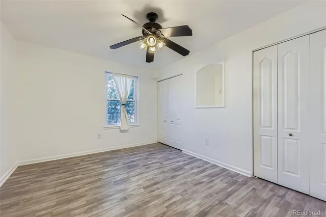 an empty room with wooden floor ceiling fan and windows