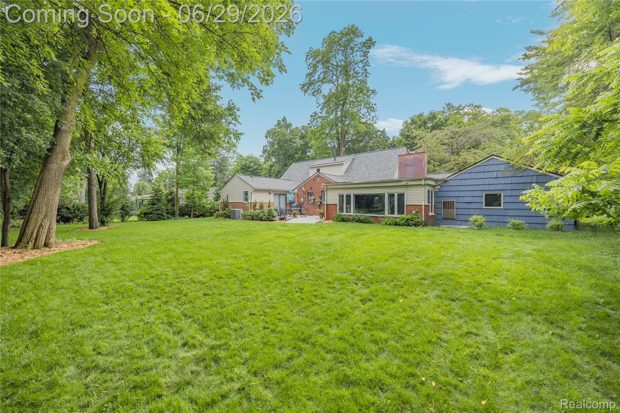 6085 Worlington Road Bloomfield Hills, MI 48301 - Photo 61 of 75 Expansive green lawn with mature trees and a multi-level dwelling featuring brick and siding exteriors, a large window bank, and a patio area