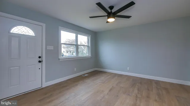 an empty room with wooden floor a ceiling fan and windows