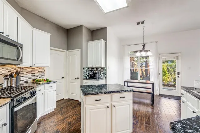 a kitchen with stainless steel appliances kitchen island granite countertop a stove a sink dishwasher and a refrigerator with wooden floor