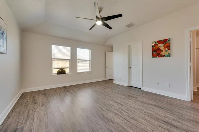 an empty room with wooden floor chandelier fan and windows