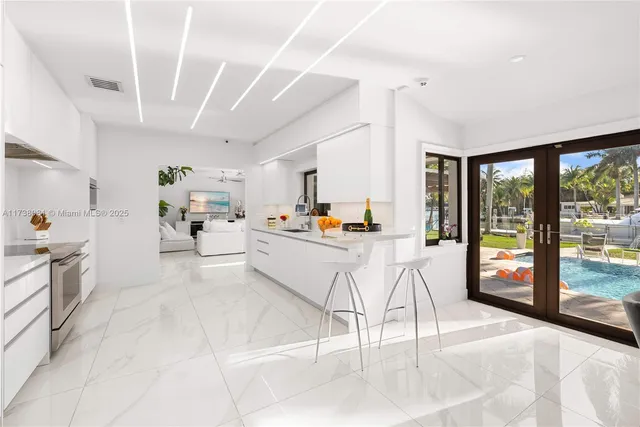 a kitchen with stainless steel appliances kitchen island granite countertop a refrigerator a stove a sink and white cabinets with island chairs