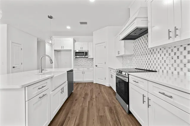 a kitchen with granite countertop a sink dishwasher stove and white cabinets with wooden floor