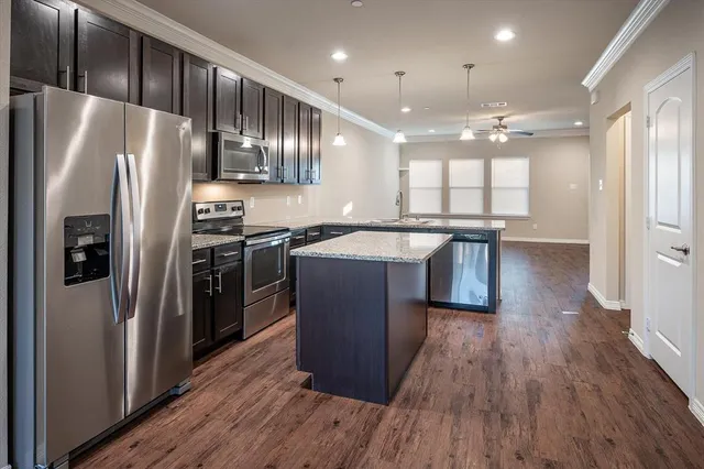 a kitchen with stainless steel appliances granite countertop a refrigerator a sink dishwasher a stove and white countertops with wooden floor