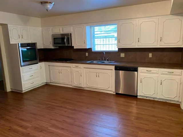 a kitchen with stainless steel appliances granite countertop white cabinets a sink a window a refrigerator and microwave