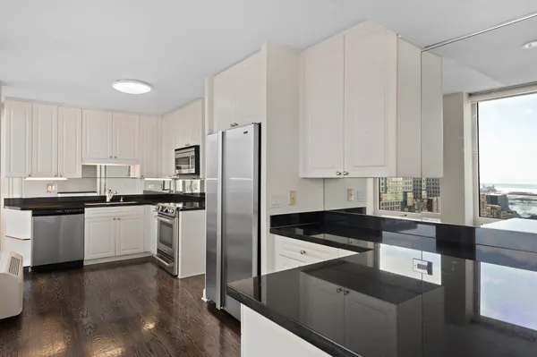 a kitchen with granite countertop a refrigerator a sink and white cabinets
