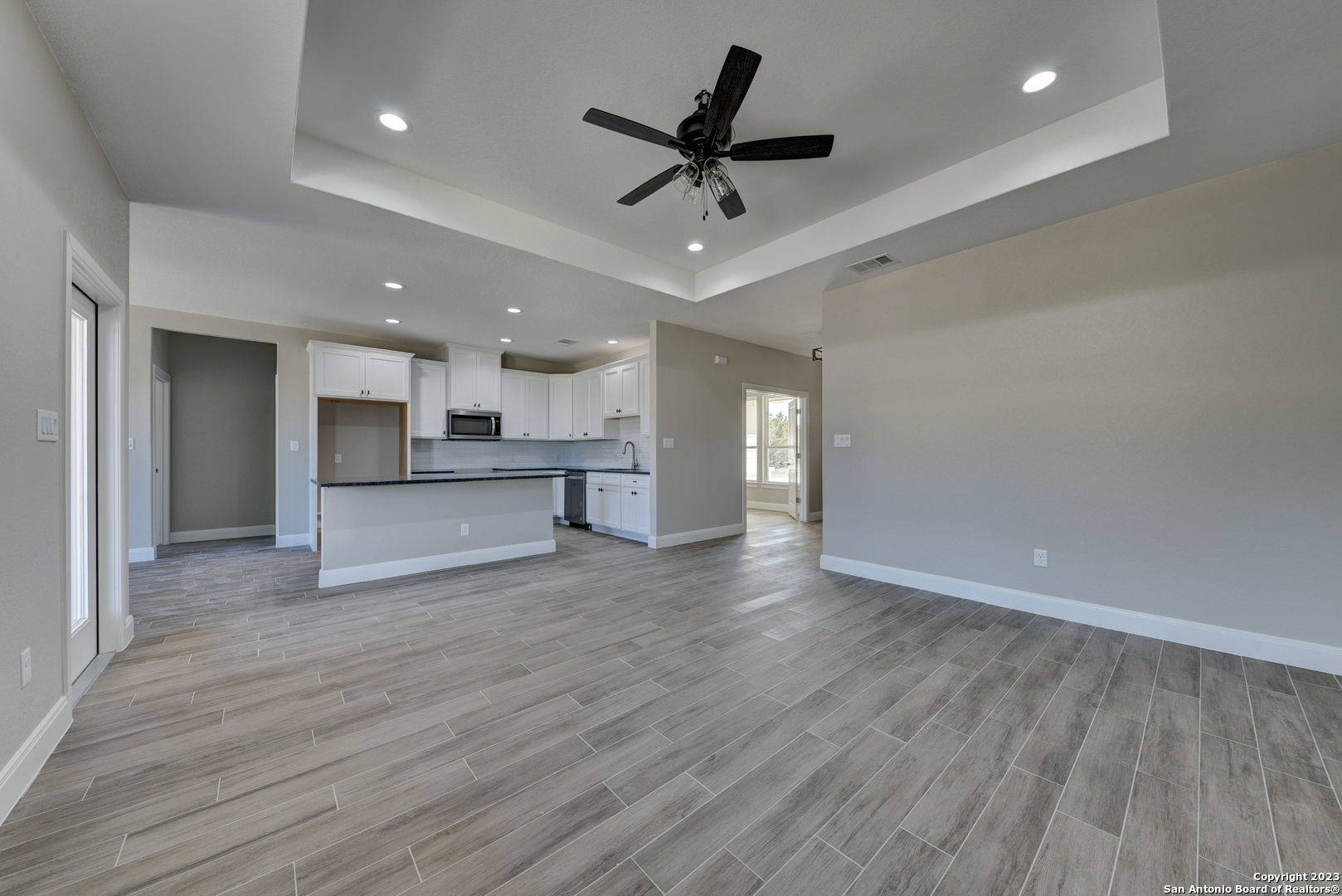 a view of an empty room and kitchen view with wooden floor and a ceiling fan