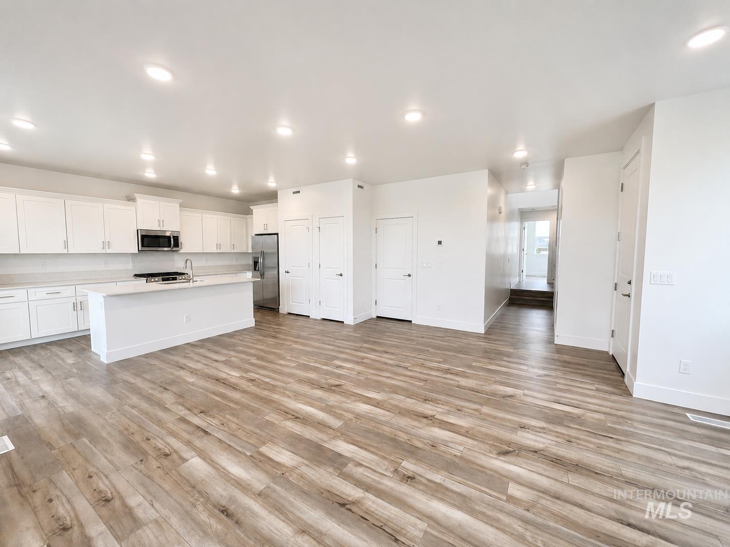 8098 West Fern Street Eagle, ID 83616 - Photo 6 of 22 Spacious interior featuring wood-finish flooring, recessed lighting, and a white kitchen with an island, stainless steel appliances, and matching cabinetry