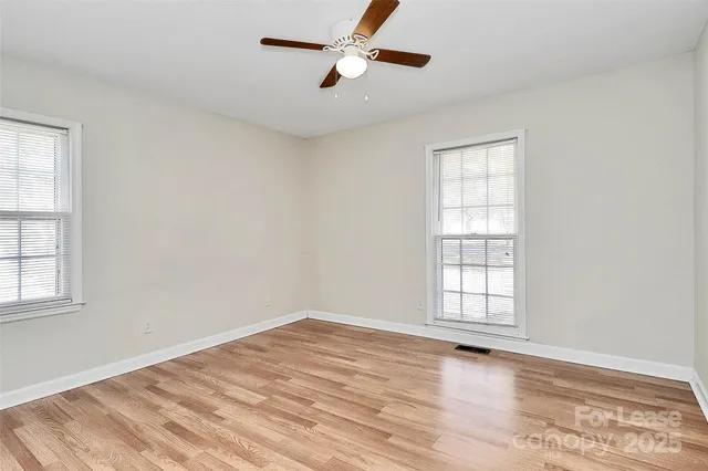 an empty room with wooden floor ceiling fan and windows