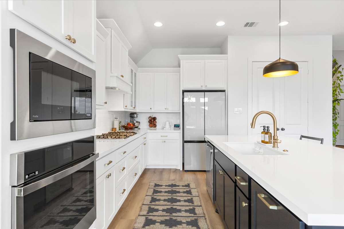 398 Trout River Road Kyle, TX 78640 - Photo 12 of 40 Two tone kitchen featuring two tone cabinets, stainless steel appliances, a kitchen island with sink, pendant lighting, and light wood-style flooring