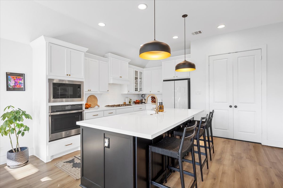 398 Trout River Road Kyle, TX 78640 - Photo 13 of 40 Two tone kitchen featuring dual tone cabinetry, a kitchen bar, stainless steel appliances, a center island with sink, and glass insert cabinets