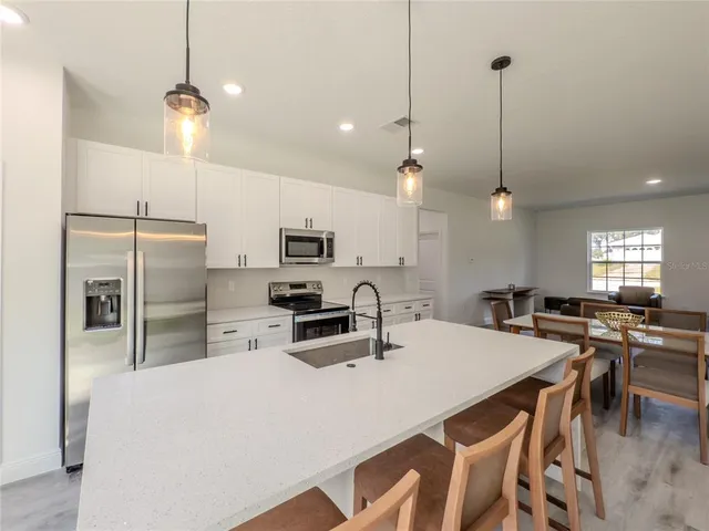 a kitchen with stainless steel appliances a stove a refrigerator a sink a center island a dining table and chairs