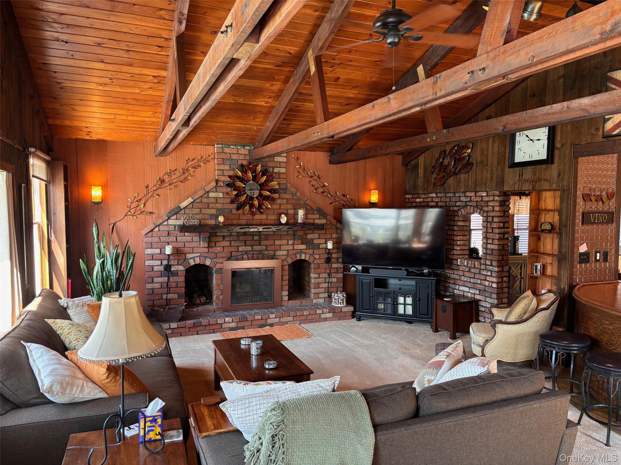 212 Matthews Road Oakdale, NY 11769 - Photo 6 of 38 Vaulted wood-paneled ceilings with exposed beams, a floor-to-ceiling brick fireplace, and wood-finish wall paneling