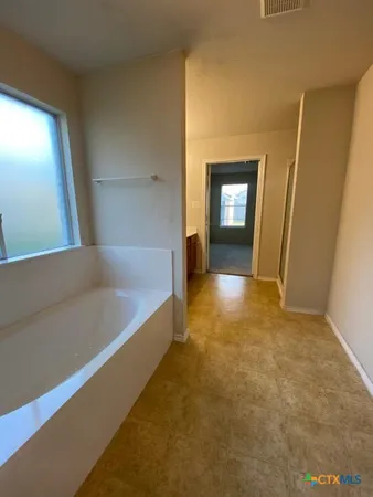 a view of a hallway to an empty room with wooden floor and a window