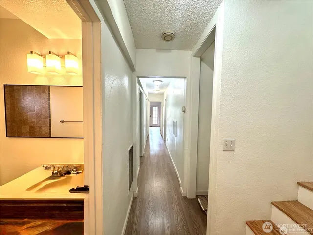 a view of a hallway with wooden floor and a bathroom