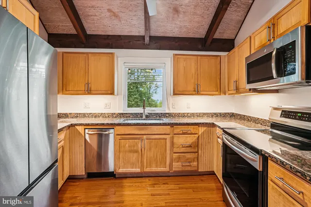 a kitchen with stainless steel appliances granite countertop a refrigerator a sink dishwasher a stove and white countertops with wooden floor