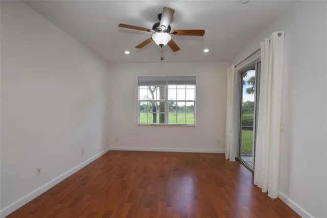an empty room with wooden floor fan and windows
