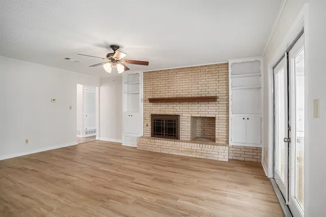 a view of an empty room with wooden floor fireplace and a window