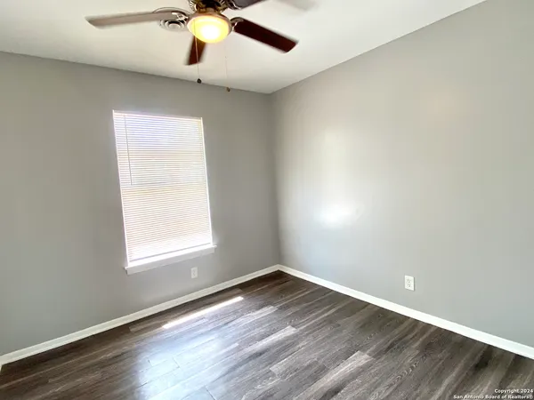 an empty room with wooden floor chandelier fan and windows