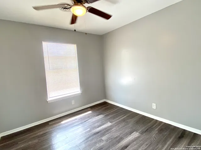an empty room with wooden floor chandelier fan and windows