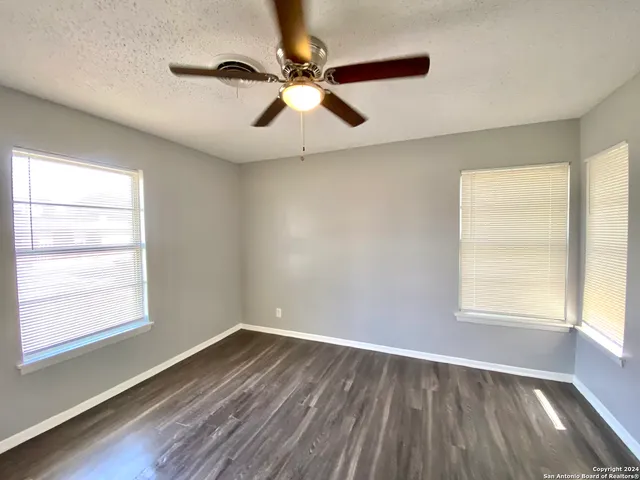 an empty room with wooden floor fan and windows