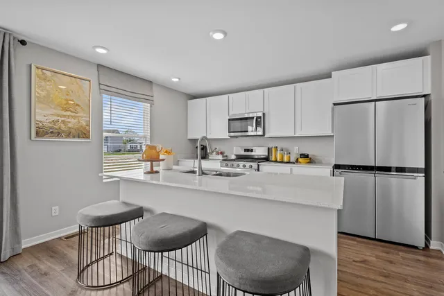 a kitchen with stainless steel appliances a refrigerator a stove a dining table and chairs with wooden floor