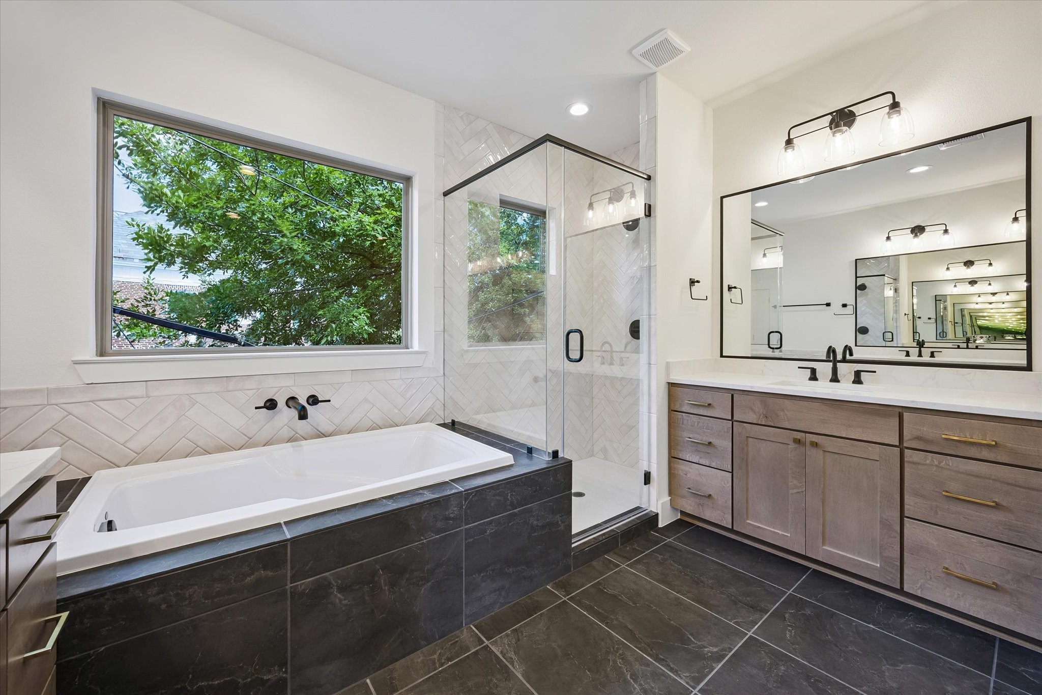 5329 Dora Street Houston, TX 77005 - Photo 25 of 43 The luxurious deep soaking tub is framed by lush greenery. The space is accented by a sleek wall-mounted spout and a stunning glass-enclosed shower, beautifully finished with intricate, floor-to-ceiling herringbone tile.