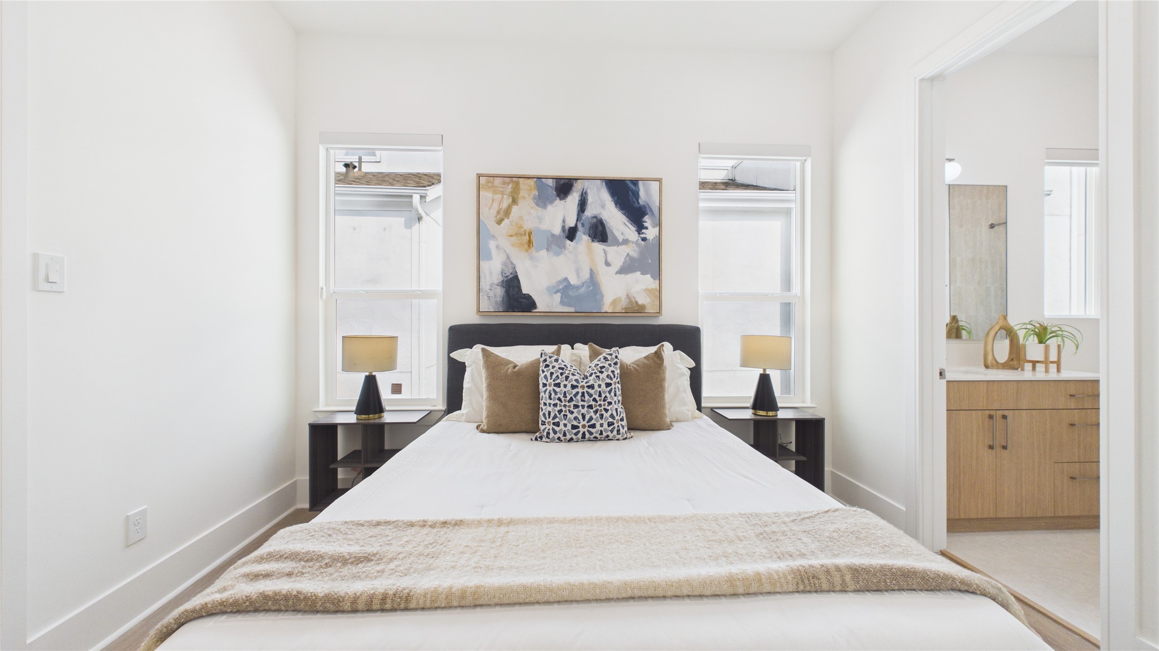 602 Skyland Terrace Way Houston, TX 77009 - Photo 22 of 40 This bright bedroom features a cozy bed with elegant pillows and a modern abstract painting. It has two bedside tables with lamps and large windows for natural light. An ensuite bathroom is visible, offering convenience and style with its sleek vanity and decor.