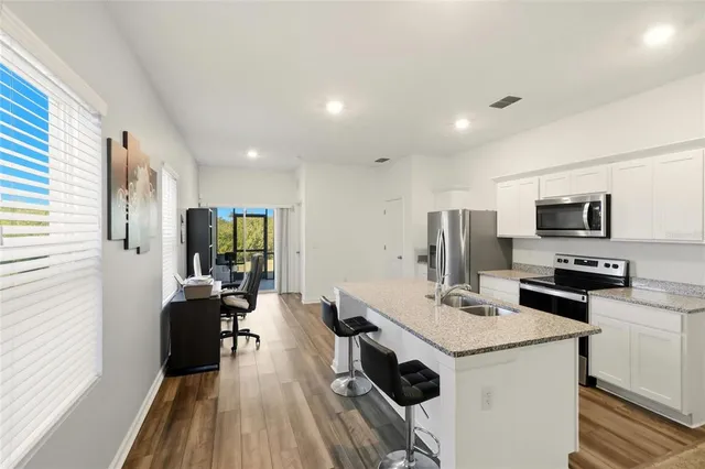 a kitchen with stainless steel appliances a stove top oven a sink a refrigerator white cabinets and wooden floor