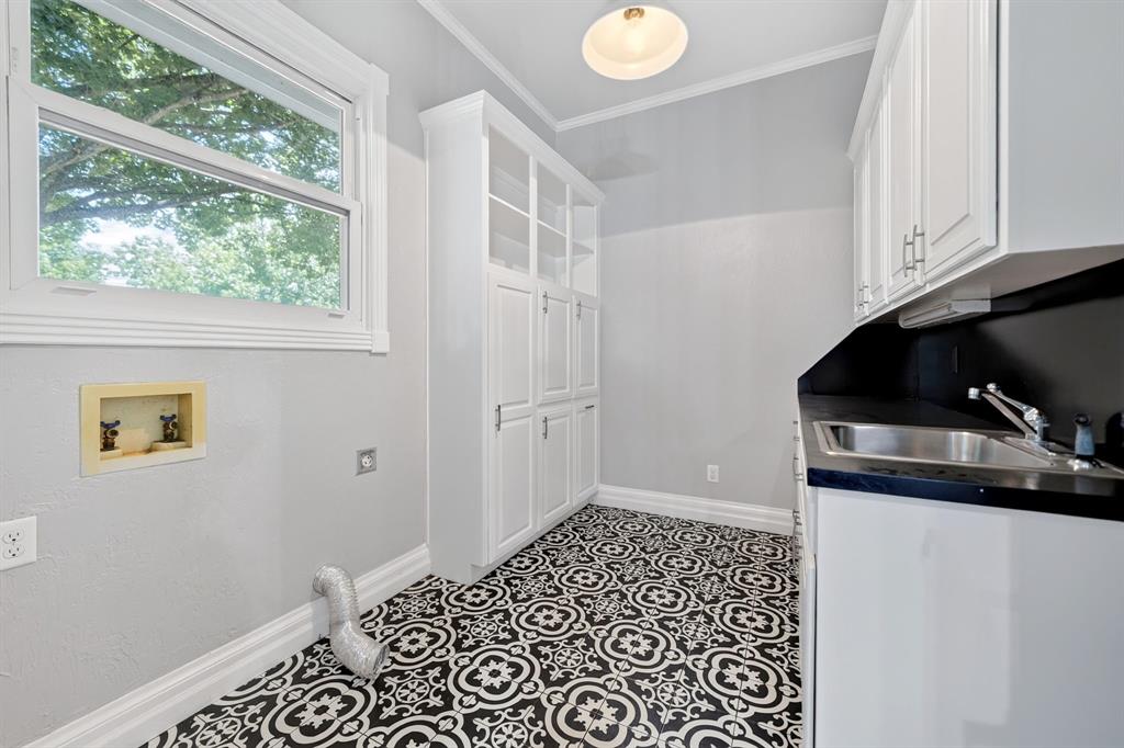 1201 Robbins Road Athens, TX 75751 - Photo 18 of 40 Laundry room featuring decorative black and white floor tiling, white built-in cabinetry, a utility sink. A window offers natural lighting and a view of the back yard area.
