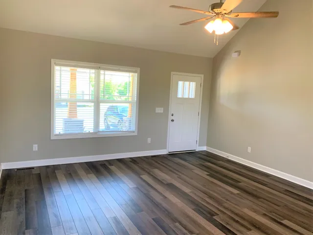 a kitchen with granite countertop a refrigerator a sink a stove and white cabinets with wooden floor