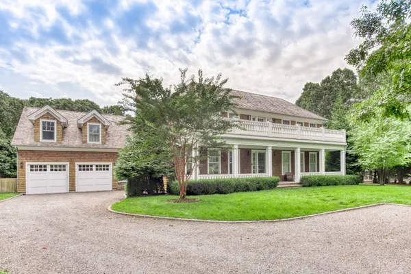 a view of a white house with a small yard and large trees