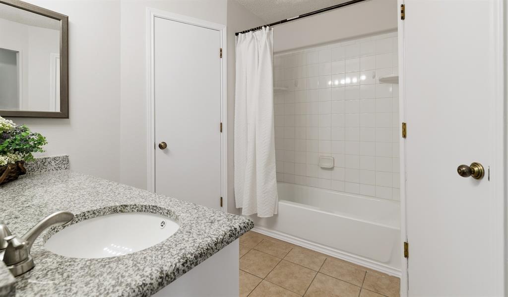 6612 Patsy Lane Watauga, TX 76148 - Photo 28 of 32 Bathroom featuring a white subway tile tub surround, an undermount sink, a granite-finish countertop, and tan tile flooring