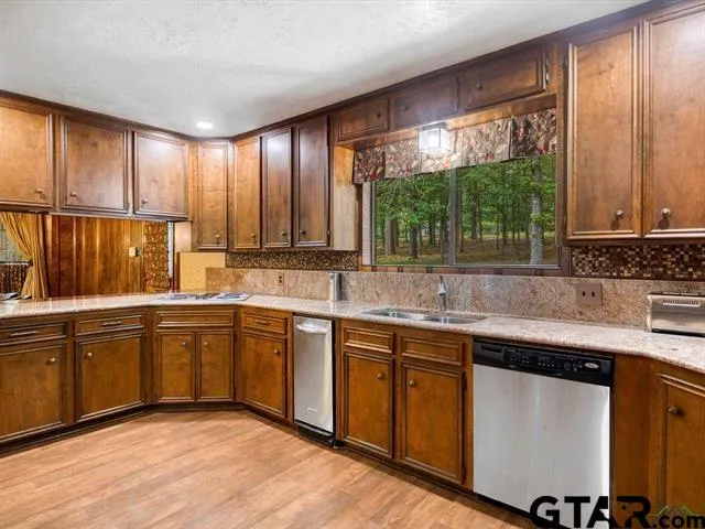 a kitchen with stainless steel appliances granite countertop wooden cabinets a sink and dishwasher with wooden floor