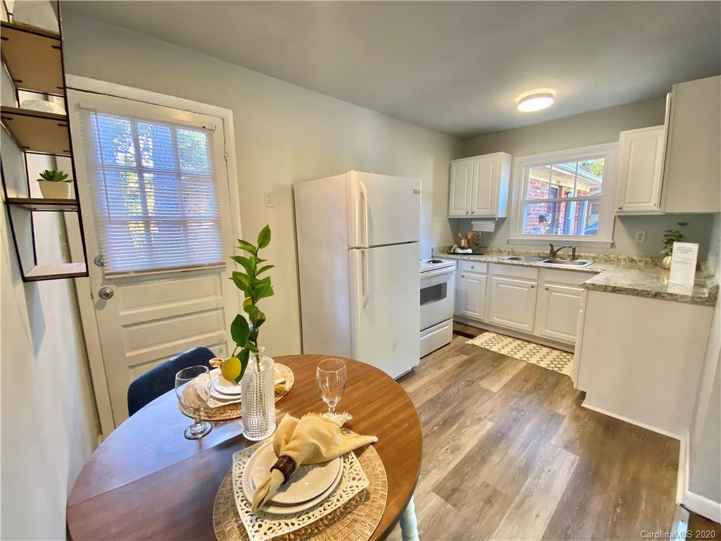 a kitchen with stainless steel appliances granite countertop a refrigerator a sink dishwasher a stove a dining table and chairs with wooden floor