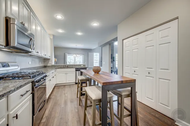 a kitchen with stainless steel appliances granite countertop a stove top oven a sink dishwasher a dining table and chairs with wooden floor