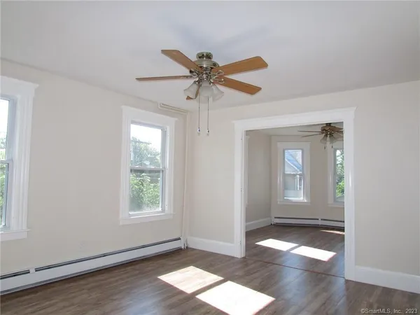 an empty room with wooden floor chandelier fan and windows