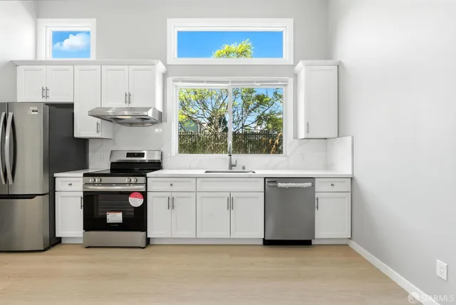 a kitchen with stainless steel appliances a stove a refrigerator sink and white cabinets
