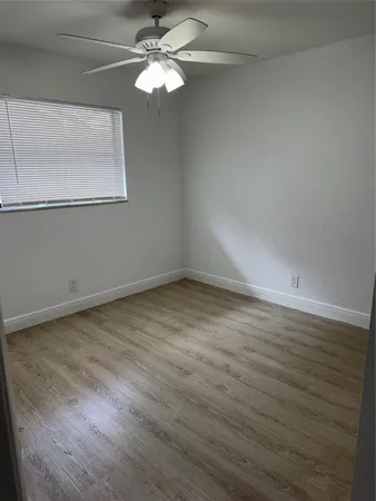 an empty room with wooden floor chandelier fan and windows