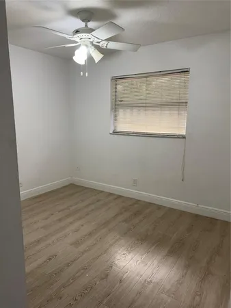 an empty room with wooden floor chandelier fan and windows