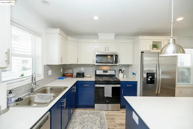 a kitchen with stainless steel appliances a sink a stove a refrigerator cabinets and a window