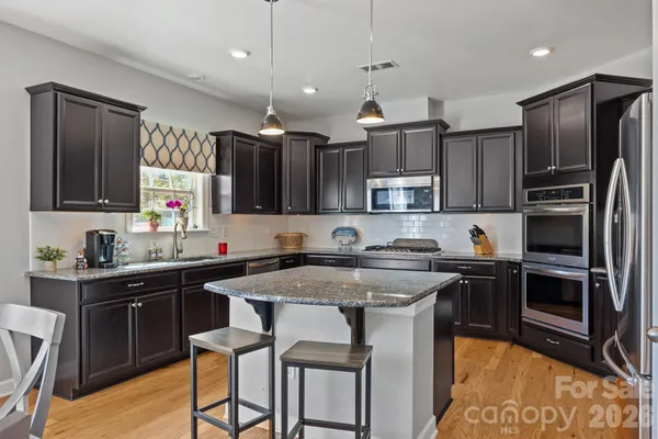 a kitchen with stainless steel appliances granite countertop a sink a stove a refrigerator and island with wooden floor