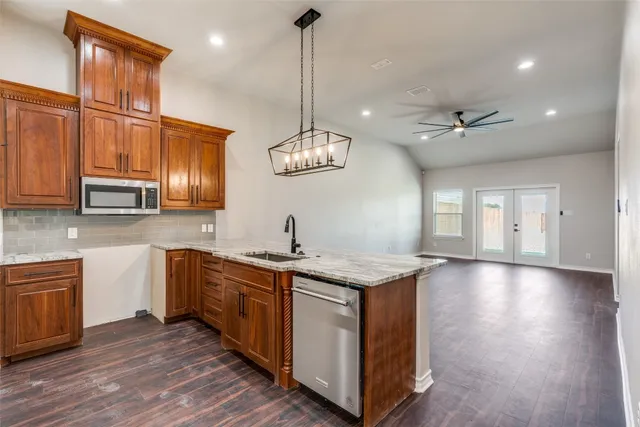 a kitchen with stainless steel appliances granite countertop wooden cabinets a stove a sink and a hard wood floors