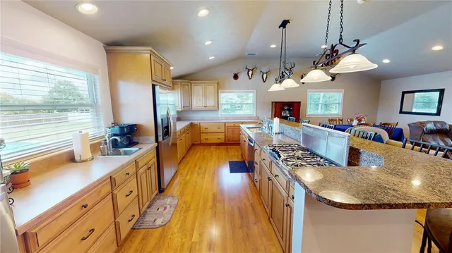 a view of a kitchen with stainless steel appliances granite countertop a sink a microwave oven and a dining table with wooden floor